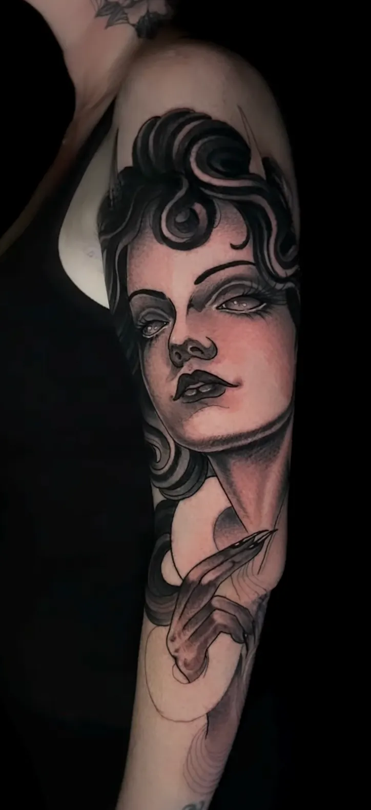 Neo-traditional portrait of a woman with dark wavy hair holding a dagger, tattooed on the upper arm in black and grey.