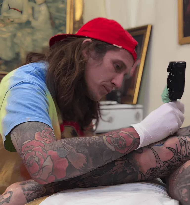 Tom Bartley tattooing, tattooed sleeves, machine in hand, mid-session in the studio.